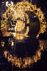 Christmas lights and wood bench, with reflection on the street, rainy night.