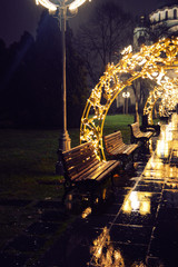 Christmas lights and wood bench, with reflection on the street, rainy night.