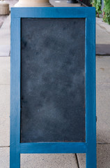 blank erased chalkboard with blue wood border sitting on a sidewalk