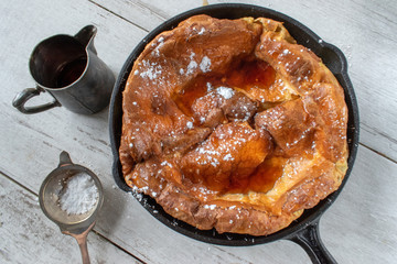 Dutch baby German pancake in cast iron pan with syrup and sugar flat lay