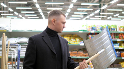 the young man chooses in store a shovel for snow removal
