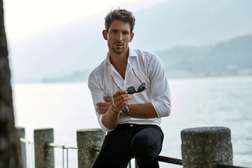 Stylish man wearing white shirt and looking at camera outdoor near the mountains