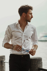 Profile portrait of stylish man wearing white shirt and holding sunglasses