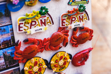 Obraz premium View of traditional tourist souvenirs and gifts from Spain, Alicante, Valencia with toys, bull figures, flamenco dancer dolls, fridge magnets with and key ring keychain, in local vendor souvenir shop