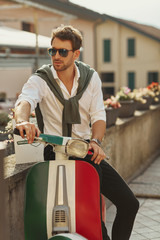 Stylish italian man wearing white shirt with tied sweater on back sitting on scooter