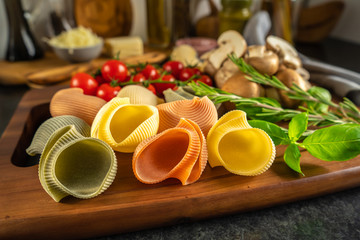 Italian pasta, colored shells, Italian colored lumaconi on a wooden board