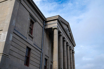 Side view of a court house building with tall pillars and windows. The sky is blue in the background with some clouds.