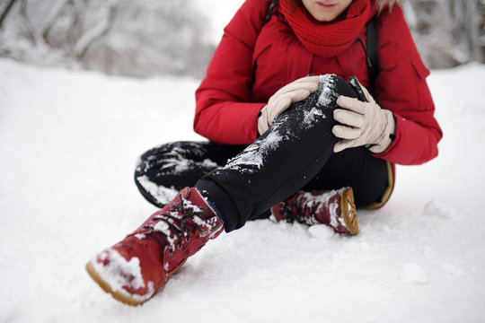 Shot of person during falling in snowy winter park. Woman slip on the icy path, fell, injury knee and sitting in the snow.