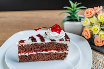 Chocolate cake with white cream and red cherry on white ceramic plate