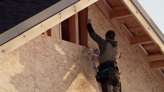 Builder is adjusting triangle plywood on its place. Frame house under construction