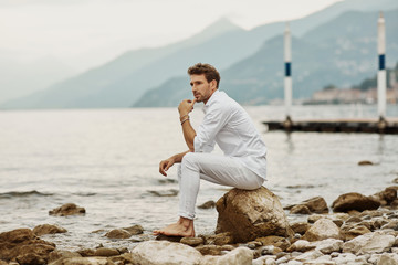 Handsome male model sits on a background of lake and mountains