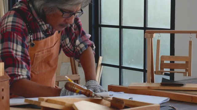 Old craftsman design his product on paper for working with wood product in the room during day time.