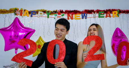 Asian couple lover holding 2020 numbers celebrating a new year at a bar shouting and laughing and Counting down to midnight on a new year party