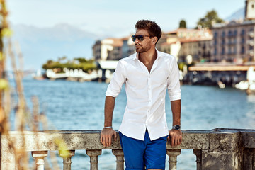 Portrait of handsome man wearing elegant white shirt and sunglasses posing outdoor over city view...