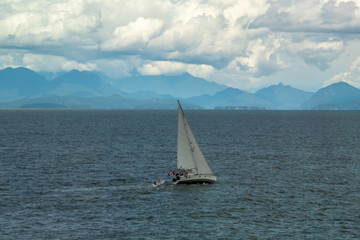 Fototapeta na wymiar Solitude - sailboat at sea, mountains and clouds