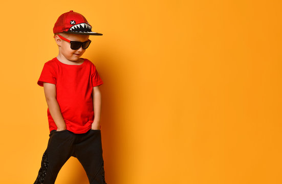 Young guy boy in a red T-shirt and dark pants, white sneakers and a funny cap posing on a free copy space on a yellow background