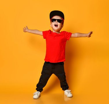 Young guy boy in a red T-shirt and dark pants, white sneakers and a funny cap posing on a free copy space on a yellow background