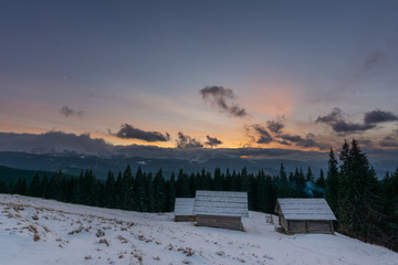 Evening dramatic sky with colorful burning clouds against the backdrop of mountain houses in winter