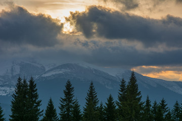 Evening dramatic sky with colorful burning clouds against the backdrop of mountain houses in winter