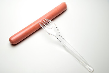 Sausage and a fork on a white background. Copy space. The concept of fast food, GMOs, hunger or lack of food. Environmental issue and the ban on plastic dishes.