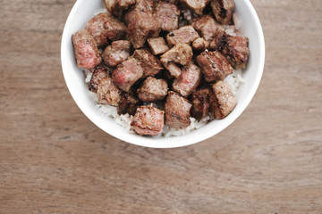 Homemade Bowl of Diced Beef Steak with rice Japanese style on wooden table.