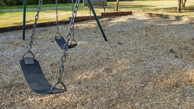 Clip of empty childrens' playground swing swinging