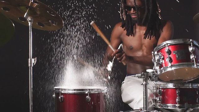 African young man plays a drum kit covered with water drops, water drops fly up spectacularly