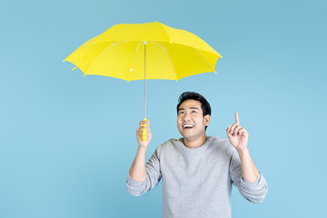 Happy Asian man holding yellow umbrella on blue background.