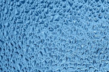 Blue decorative glass with a relief embossed pattern in the form of small pits or grooves. Glass glare background, texture. Color of the year 2020 concept