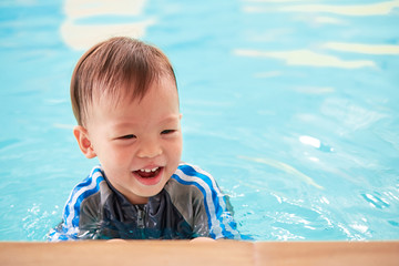 Asian 2 years old toddler boy child on the edge of a swimming pool, little kid takes a swimming lesson in indoor swimming pool