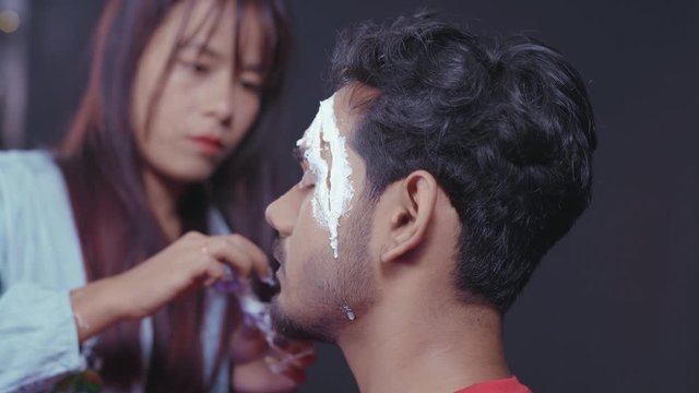 Make up artist preparing man's face for Halloween mask by putting white prosthetic insert on his eye 