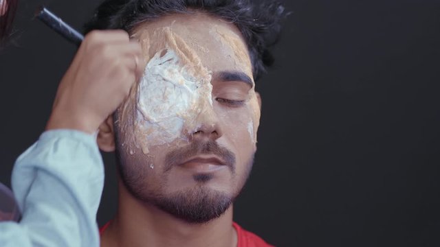 Make up artist starting coloring mask on man's face to make a Halloween mask 