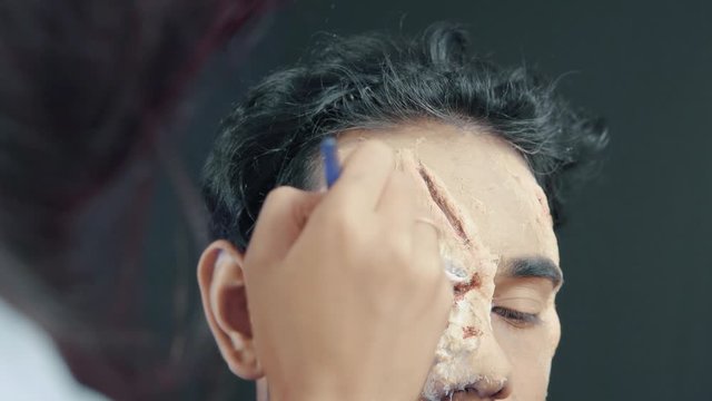 Make up artist coloring prosthetic insert on man's face and making a Halloween mask 