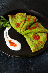 Classic thin green spinach pancakes with sour cream and red caviar in a black plate.