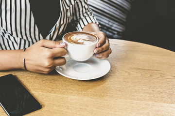 businesswomen working with laptop and hand catch cup of coffee. A mobile phone is on the table near the laptop.