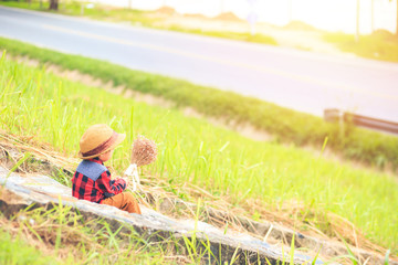 a children wear hat and sitting on stair. A children hold flower and near the road.