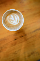 Top view of coffee in a paper cup with heart shaped whipped cream. The background is a wooden table for copy space.