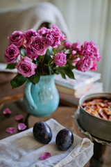 A bouquet of pink roses on a table in a jug and a plum cake near