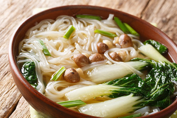 Spicy rice noodle soup with mushrooms, Asian spices and bok choy closeup in a bowl. horizontal