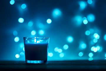 Silhouette of burning candle with a golden blurred lights on dark background, blue toned photo