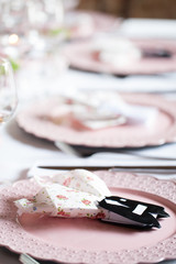 Pink themed festive wedding table setting and decoration with pink flowers, napkins, glasses and candles, vintage cutlery, resulting in a bright summer table decor