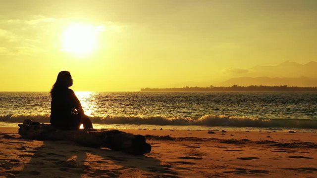 Philippines, golden hour light over the sandy beach, woman watching sunset