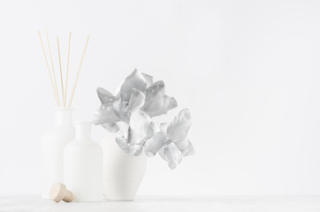 Elegant blank white glass bottles with aromatic sticks on soft light white wood table with silver decorative leaves as modern elegant home decor.