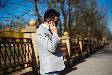 Young successful handsome man in a gray jacket is standing on the street