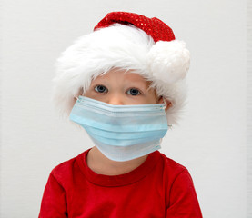 Portrait A child, a toddler in a red santa hat is sick at Christmas, is protected from viruses by a white scarf as a medical mask on a white background. The flu epidemic for the holidays.