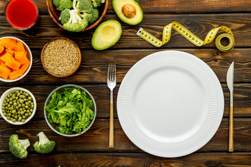 Diet program concept. Empty plate, measure tape and vegetables on dark wooden background top view mockup