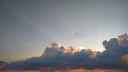 The beautiful sunset behind the clouds and the light shining behind the clouds in the evening of the day.