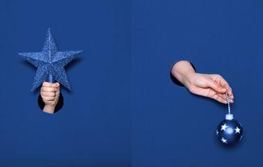 A hand in the holes on paper holds a Christmas ball and a Christmas star. Classic blue paper...