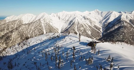 Actionsportlers were dropped by a helicopter at the top of the mountains. The sun is shining brightly in the blue sky. There is a mountain range in the background covered in snow. Drone shooting.