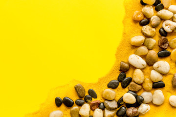 Sea rest, summer vacation concept. Stones and sand on yellow background top-down frame copy space